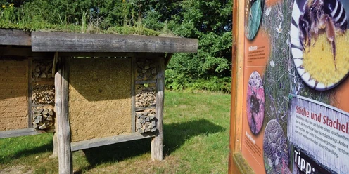 Insektenhotel mit informativer Schautafel Insektenhotel mit natürlichen Baumaterialien, flankiert von einer Schautafel zur Insektenwelt.