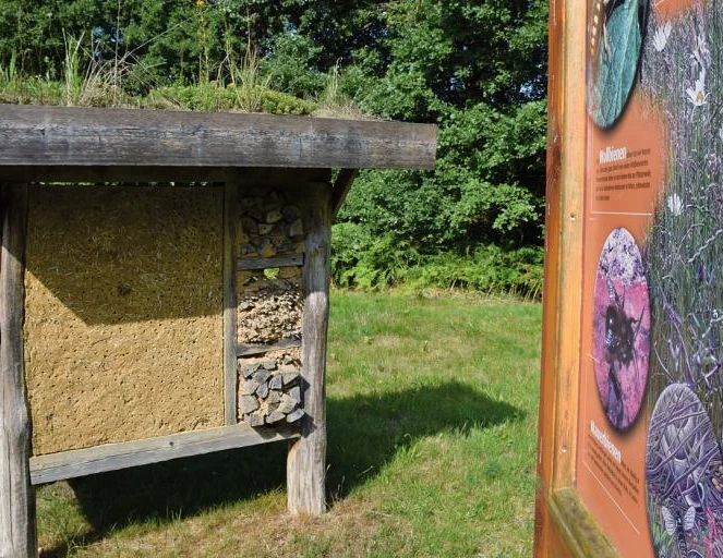 Insektenhotel mit informativer Schautafel Insektenhotel mit natürlichen Baumaterialien, flankiert von einer Schautafel zur Insektenwelt.