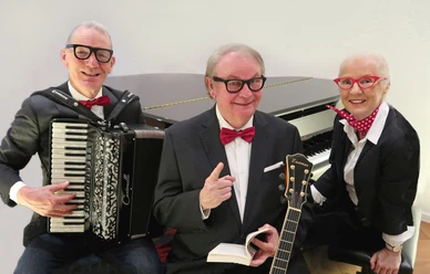 Drei lächelnde Künstler mit Akkordeon, Buch und Gitarre vor einem Flügel