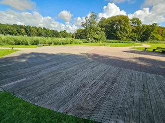 Breite Holz- und Pflasterfläche im Gesundheitspark Speckenbüttel mit Bänken und viel Grün.