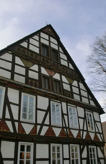 Fachwerkhaus mit verziertem Giebel und historischen Fenstern an einem sonnigen Kirchplatz in Ottbergen.