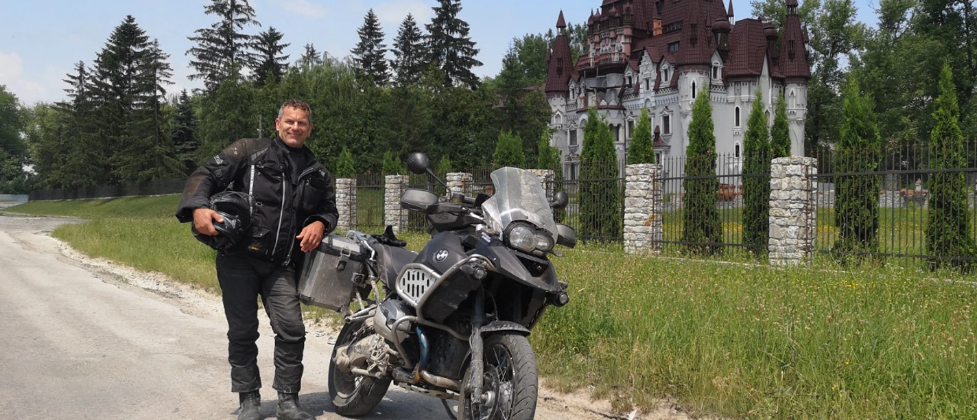 Mann mit Motorradmontur steht vor seinem Motorrad vor einem prunkvollem Gebäude