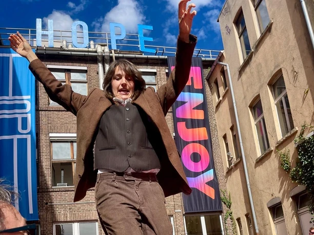 Performer mit erhobenen Armen auf Tisch vor Publikum im Kölner Innenhof mit HOPE-Schriftzug