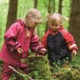 Kinder entdecken den Wald Zwei Kinder in Regenkleidung erforschen einen moosbedeckten Baumstamm im grünen Wald.