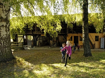 Kinder rennen vor Hütte Kinder rennen fröhlich über eine Wiese vor einer rustikalen Holzhütte, umgeben von Bäumen im Herbst.