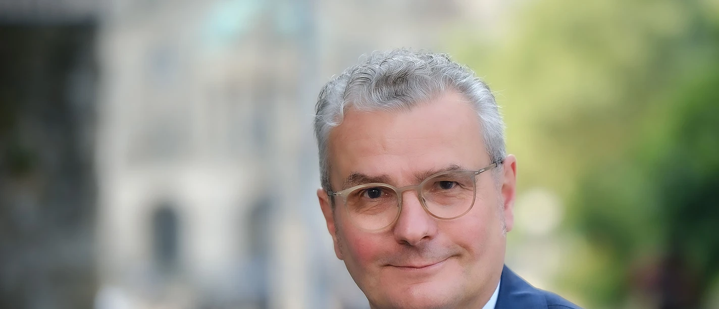 Freundlich lächelndes Porträt von Hans-Joachim Lenke im blauen Anzug mit Krawatte und Brille.