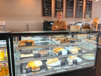 Mitarbeiterin hinter einer Glasvitrine mit Kuchen und Snacks im Café Zerino Coffee.