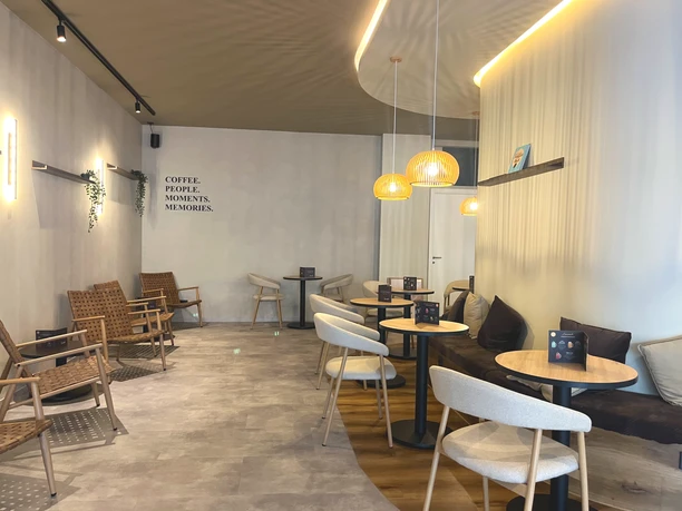 Modernes Interieur des Cafés Zerino Coffee mit hellen Stühlen, runden Tischen und einer Sitzbank.