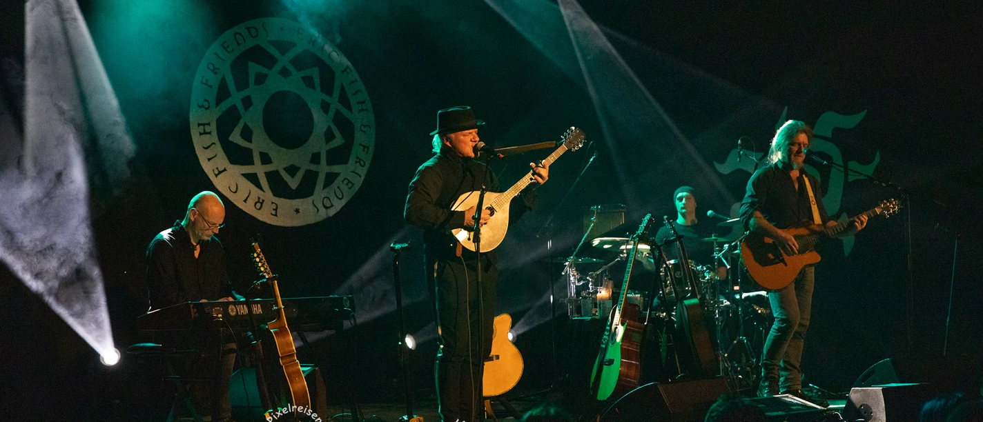 ERIC FISH & FRIENDS live Vier Musiker spielen bei einem Live-Konzert auf einer beleuchteten Bühne vor Publikum.