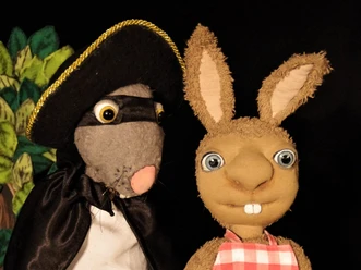 Raeuber Ratte Zwei Handpuppen stehen nebeneinander: eine als Räuber verkleidete Figur und ein Hase mit kariertem Latz.