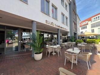 Außenterrasse von Elijel's Café am Kolbeplatz mit weißen Möbeln und grünen Palmen.