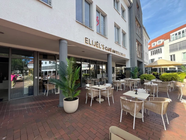 Außenterrasse von Elijel's Café am Kolbeplatz mit weißen Möbeln und grünen Palmen.