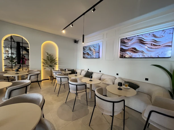 Elijel's Helles Café-Interieur mit weißen Möbeln und zwei großen, beleuchteten abstrakten Wandbildern.