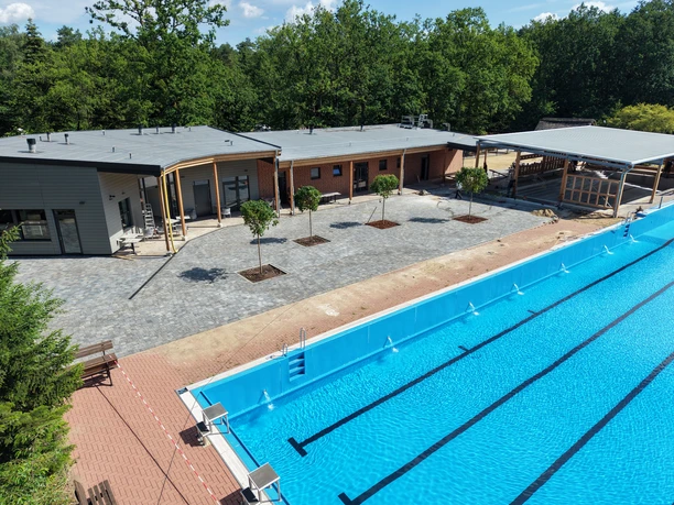 Schwimmbecken im Waldbad Amelinghausen mit Gebäuden, Terrasse und Bäumen.