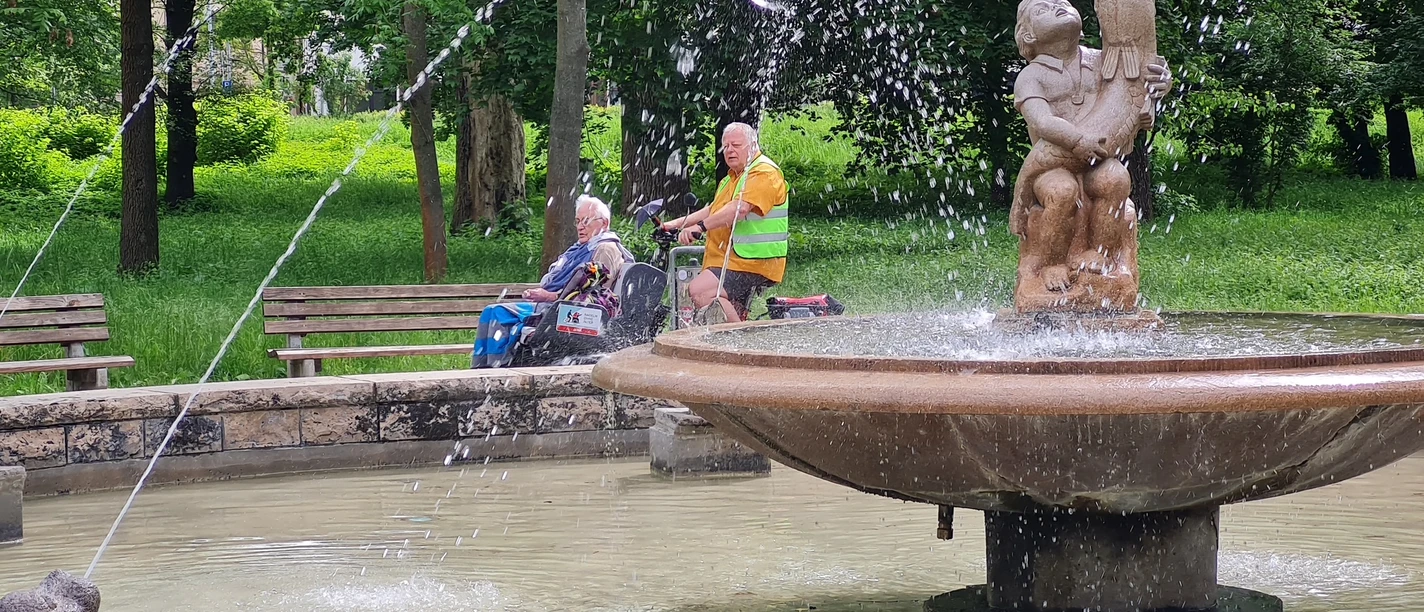 Brunnen in der Oberaue Jena, dahinter fährt eine Fahrradrikscha