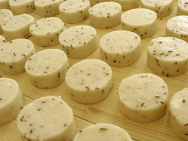 Nieheim, Nieheimer Käse Runde Käselaibe mit Kümmel liegen auf hölzerner Oberfläche, angeordnet in symmetrischen Reihen.