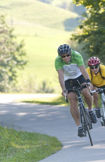 Rasante Abfahrt Zwei Radfahrer in sportlicher Haltung fahren eine kurvige Landstraße hinunter, umgeben von Bäumen.
