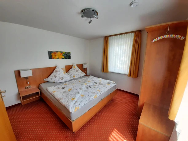 Schäferhaus Willingen, Schlafzimmer Schlafzimmer mit Doppelbett, Holzschrank, Nachttischen und orangefarbenen Vorhängen