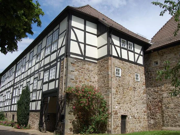 Domänenburg Aerzen Fachwerkgebäude der Domänenburg Aerzen mit steinernem Erdgeschoss und blühendem Strauch im Vordergrund.