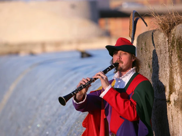 Rattenfänger an der Weser Ein Musiker in traditionellem Kostüm spielt die Klarinette an einem Fluss mit historischen Gebäuden.
