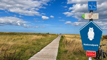 Nationalpark-Schild am Strandweg in Schillig mit Bohlenweg und Fahrrad