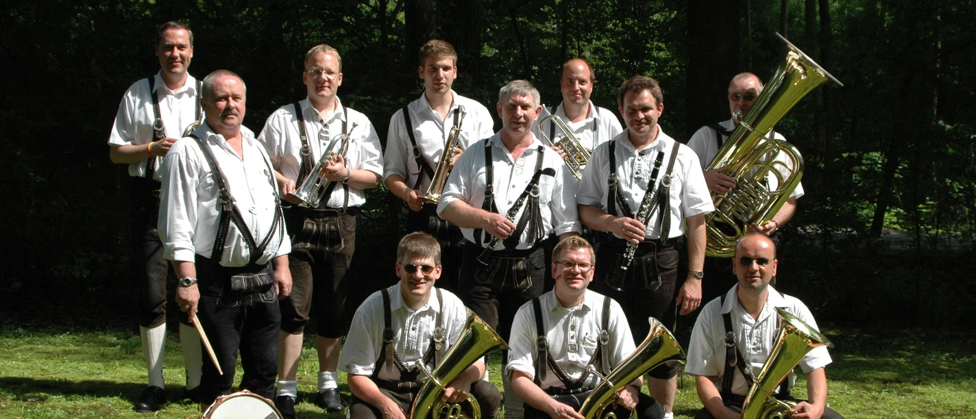 Blaskapelle in bayerischer Tracht mit Instrumenten auf einer Wiese vor einem Wald.
