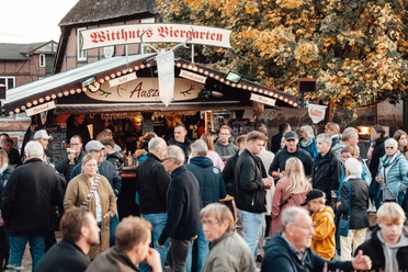 Besucher vor einem Biergartenstand auf dem Herbstmarkt unter buntem Laub.