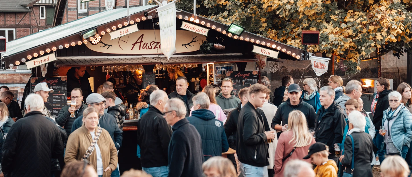 Besucher vor einem Biergartenstand auf dem Herbstmarkt unter buntem Laub.