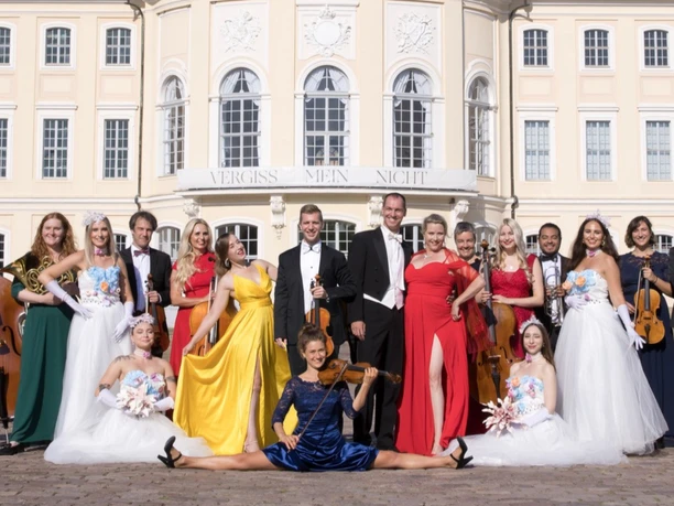 Die große Johann Strauss Revue Ensemble der Johann Strauss Revue vor prächtiger Schlossfassade mit Streichinstrumenten.