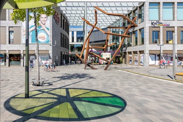 A sunny spot at the Kulturforum Hanau with a glass roof, an art sculpture, and the Forum Hanau