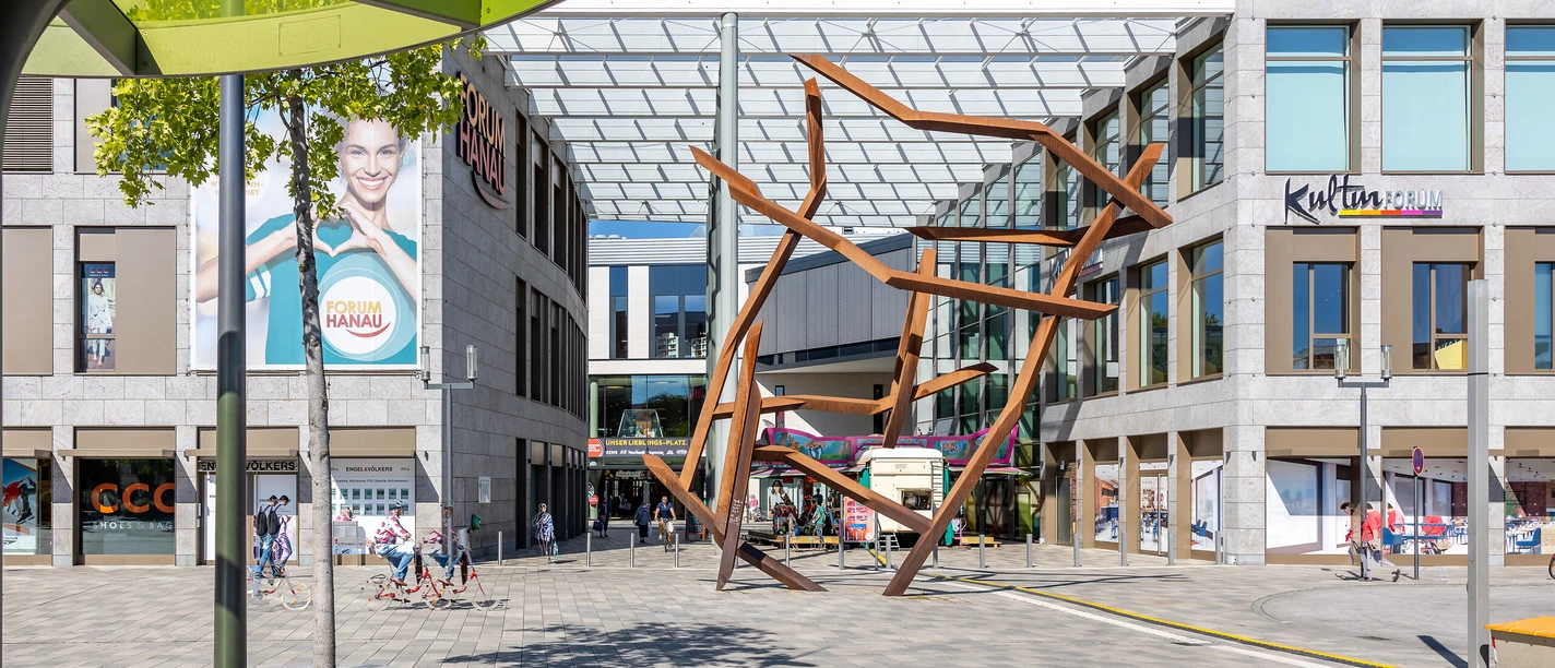 A sunny spot at the Kulturforum Hanau with a glass roof, an art sculpture, and the Forum Hanau