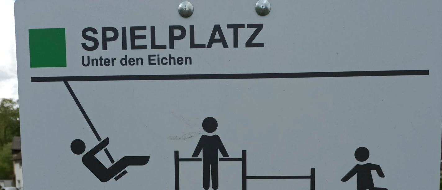Schild „Spielplatz Unter den Eichen“ mit Piktogrammen für Schaukel und Spielgeräte.