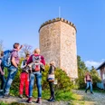 Eine Gruppe von Wanderern steht vor einem historischen, runden Steinturm in sonniger Umgebung.