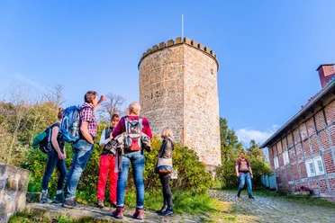Wandergruppe an der Burg Ravensberg Eine Gruppe von Wanderern steht vor einem historischen, runden Steinturm in sonniger Umgebung.