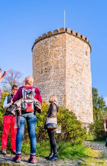 Wandergruppe an der Burg Ravensberg Eine Gruppe von Wanderern steht vor einem historischen, runden Steinturm in sonniger Umgebung.