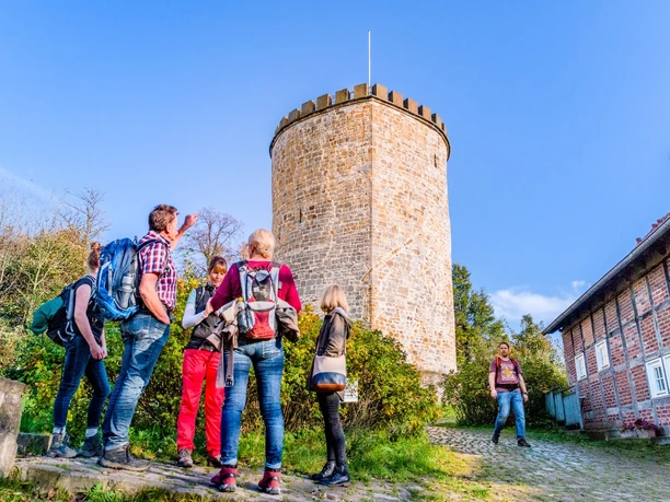 Wandergruppe an der Burg Ravensberg Eine Gruppe von Wanderern steht vor einem historischen, runden Steinturm in sonniger Umgebung.