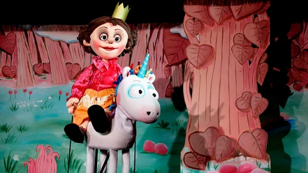 Prinzessin-Puppe reitet auf weißem Einhorn vor einer bunten Waldkulisse