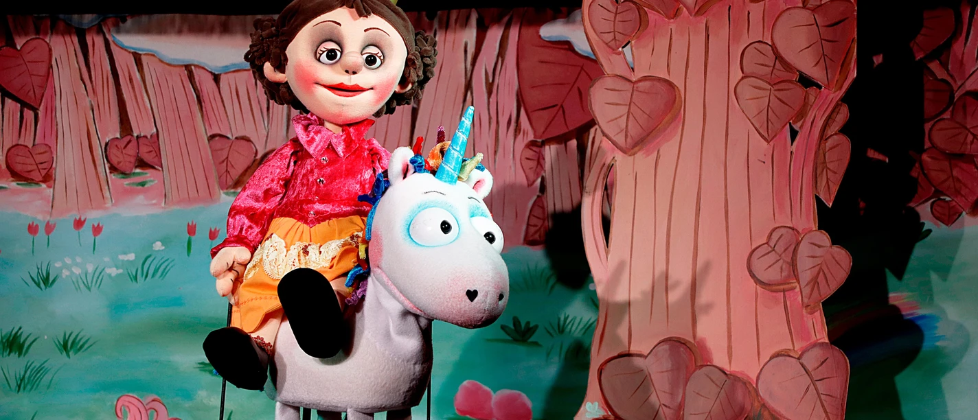 Prinzessin-Puppe reitet auf weißem Einhorn vor einer bunten Waldkulisse