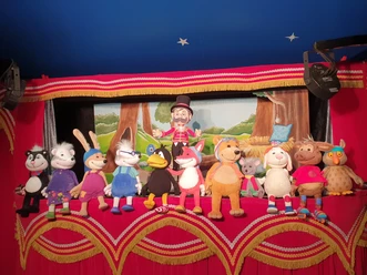 Bunte Handpuppen um den kleinen Raben Socke auf rot-goldener Puppentheaterbühne