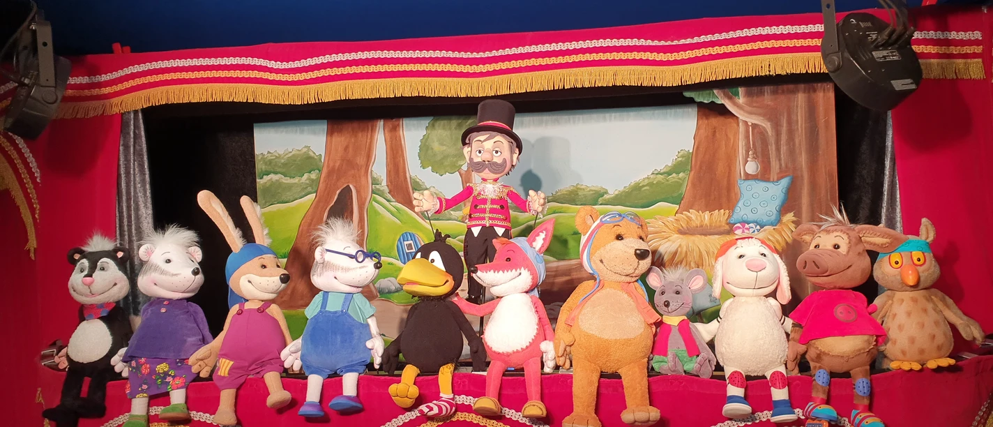 Bunte Handpuppen um den kleinen Raben Socke auf rot-goldener Puppentheaterbühne