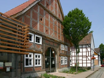 Ein traditionelles Fachwerkhaus mit Backsteinmusterung steht neben modernem Glasbau unter blauem Himmel.