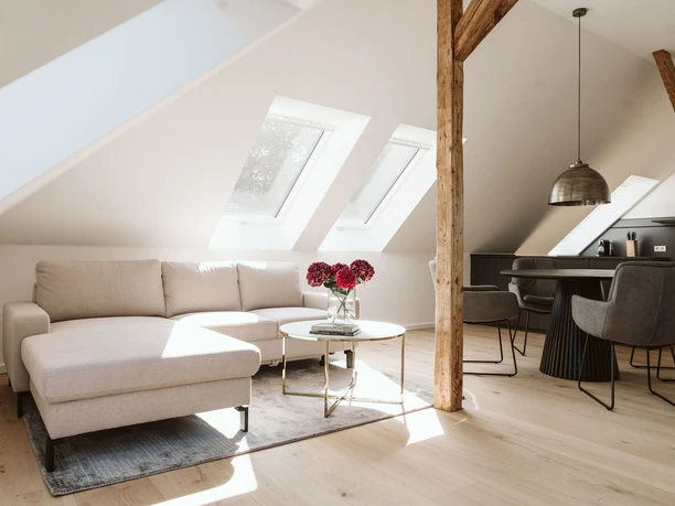 Villa am Stadtpark Heller Wohn- und Essbereich mit L-Sofa, Holzbalken und Dachfenstern in der Villa am Stadtpark.
