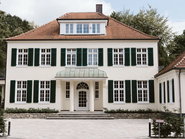 Villa Stadtpark Weiße Villa am Stadtpark mit grünen Fensterläden und rotem Ziegeldach.