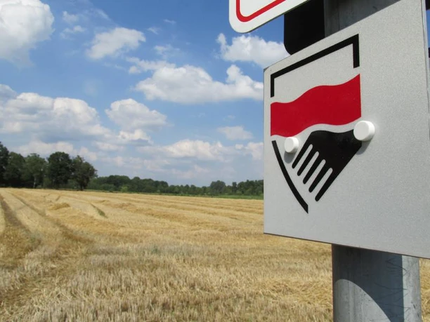 Rund um Greffen Ein Schild mit rotem Symbol steht vor einem goldenen Getreidefeld unter blauem Himmel.