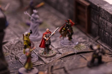 Bemalte Fantasy-Spielfiguren auf einem Tabletop-Spielfeld mit Steinmauern.