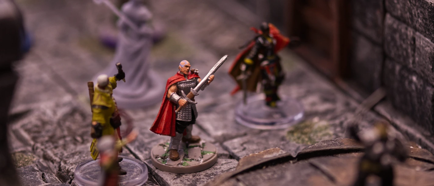 Bemalte Fantasy-Spielfiguren auf einem Tabletop-Spielfeld mit Steinmauern.