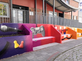 Bunte Treppenfassade mit Graffiti von Mikrofon, Gamecontroller und Spielfiguren.