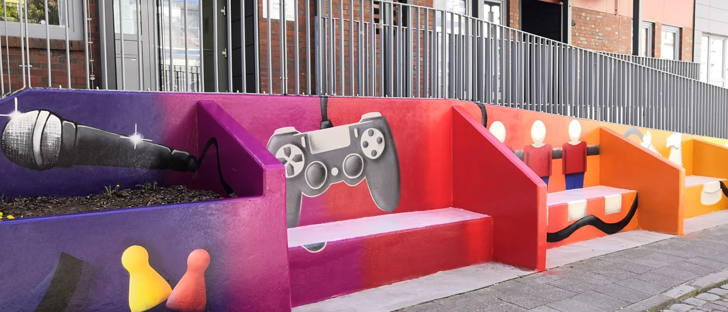 Bild1 Fassade (c) Lehe-Treff_WEB.jpg Bunte Treppenfassade mit Graffiti von Mikrofon, Gamecontroller und Spielfiguren.