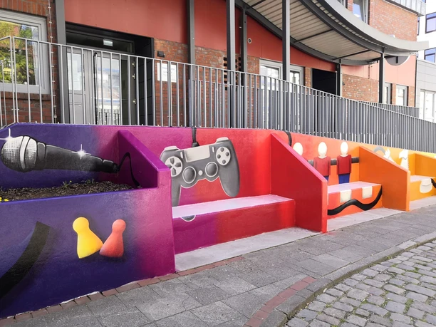 Bunte Treppenfassade mit Graffiti von Mikrofon, Gamecontroller und Spielfiguren.