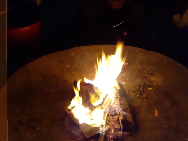 Ein Lagerfeuer in einer runden Feuerstelle. Flammen leuchten in der Dunkelheit.